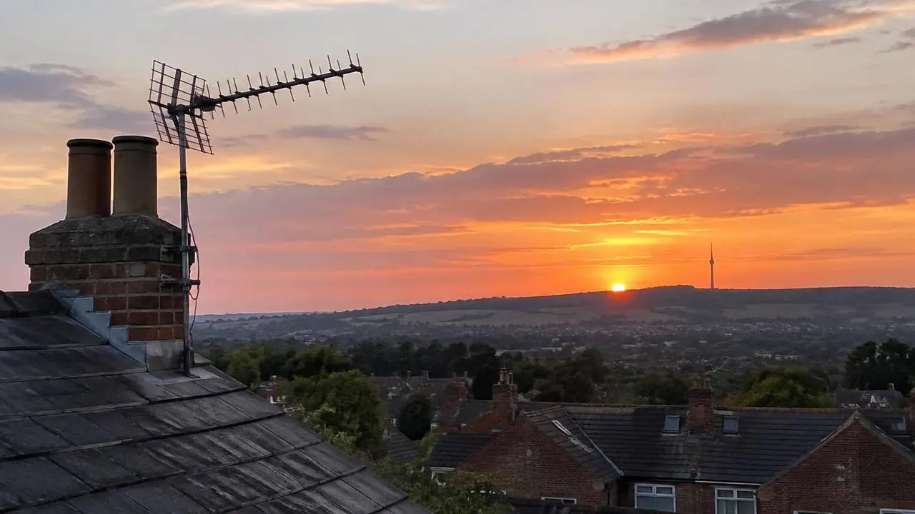Rooftop TV aerial at sunset pointing towards a distant transmitter mast